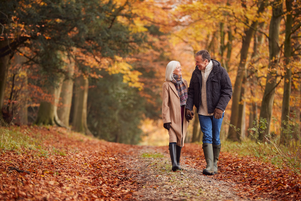 A happy senior couple going for a walk through a park during the fall season